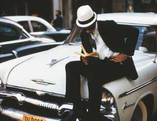 A sharply-dressed young man sitting on a Plymouth car and reading a book, New York City, June 1962. (Photo by Ernst Haas/Hulton Archive/Getty Images)